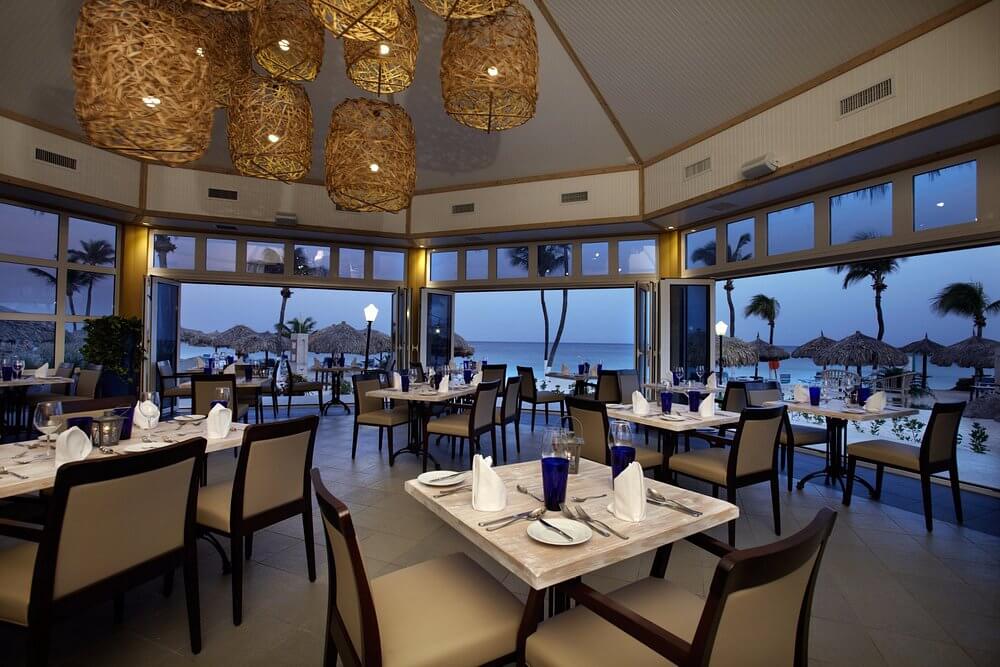 Outdoor palapa dining tables on the sand at Water's Edge Restaurant & Bar in Aruba.