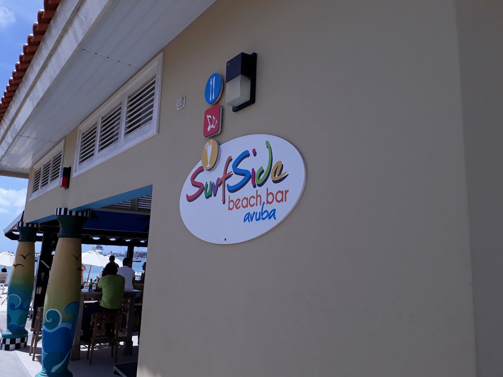 Surfside Beach Bar sign mounted on the exterior wall with the beach seating area visible in Aruba.