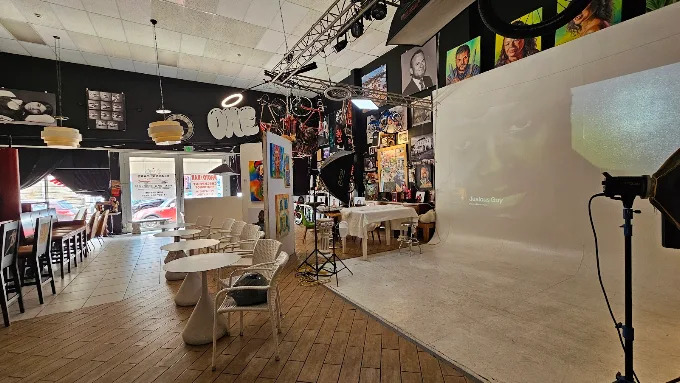 Studio interior in Aruba showing a white seamless photography backdrop with studio lighting equipment alongside a cafe seating area with small white tables and chairs.