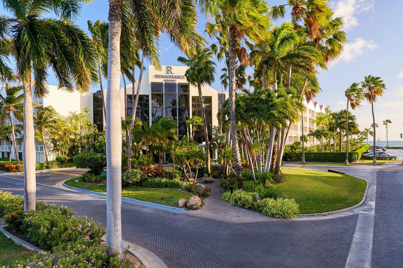 Exterior of Renaissance Wind Creek Aruba Resort in Aruba with palm trees, landscaped gardens, resort buildings, and a driveway entrance.