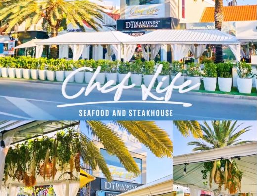Chef Life Aruba Restaurant exterior with palm trees, covered outdoor dining areas, white tables, and restaurant signage.