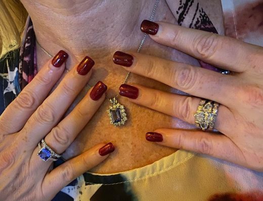 A woman holding her hands to her chest showcasing a gemstone pendant necklace and diamond rings at Eternity Fine Jewels in Aruba.