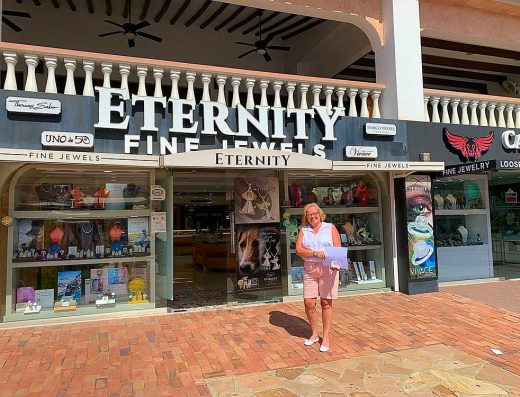 A woman standing in front of the Eternity Fine Jewels store entrance in Aruba.