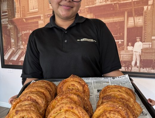 Old Dutch Bakery staff member in Aruba holding a tray filled with round spiral pastries.