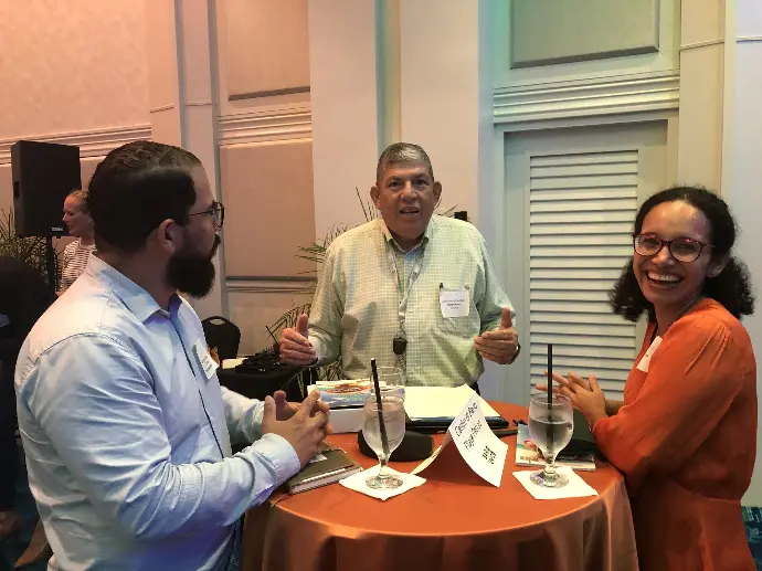 Three adults seated around a table during an indoor gathering associated with Centro di Bario Playa Pabao in Aruba.